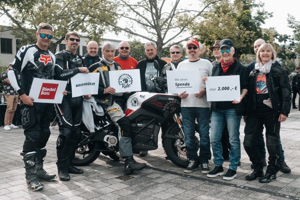 12 Personen in Motorraduniform halten eine Spende in der Hand